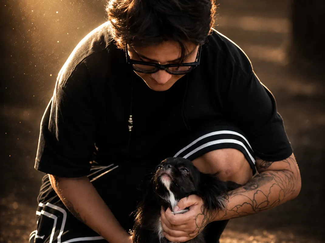 Una persona accovacciata tiene tra le mani un Chihuahua nero a pelo lungo, nella luce calda del tramonto
